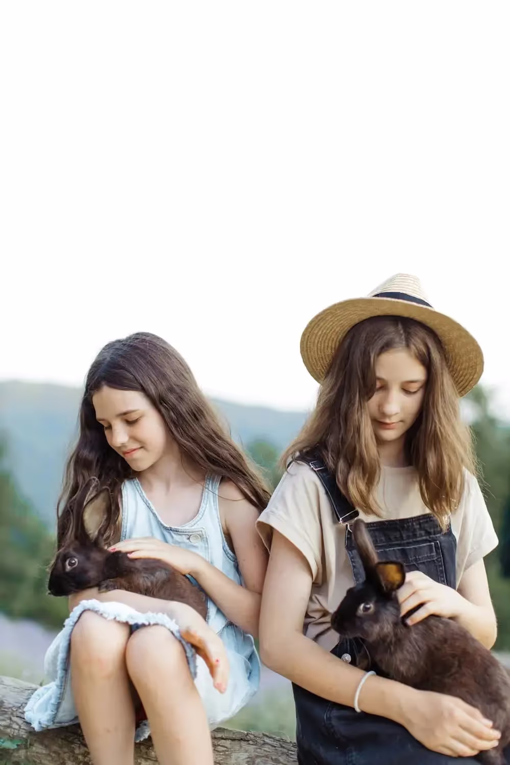 Two girls sitting outdoors each holding a pet rabbit