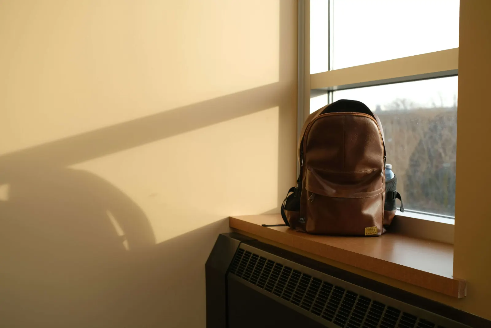 Brown leather backpack resting on a sunlit windowsill