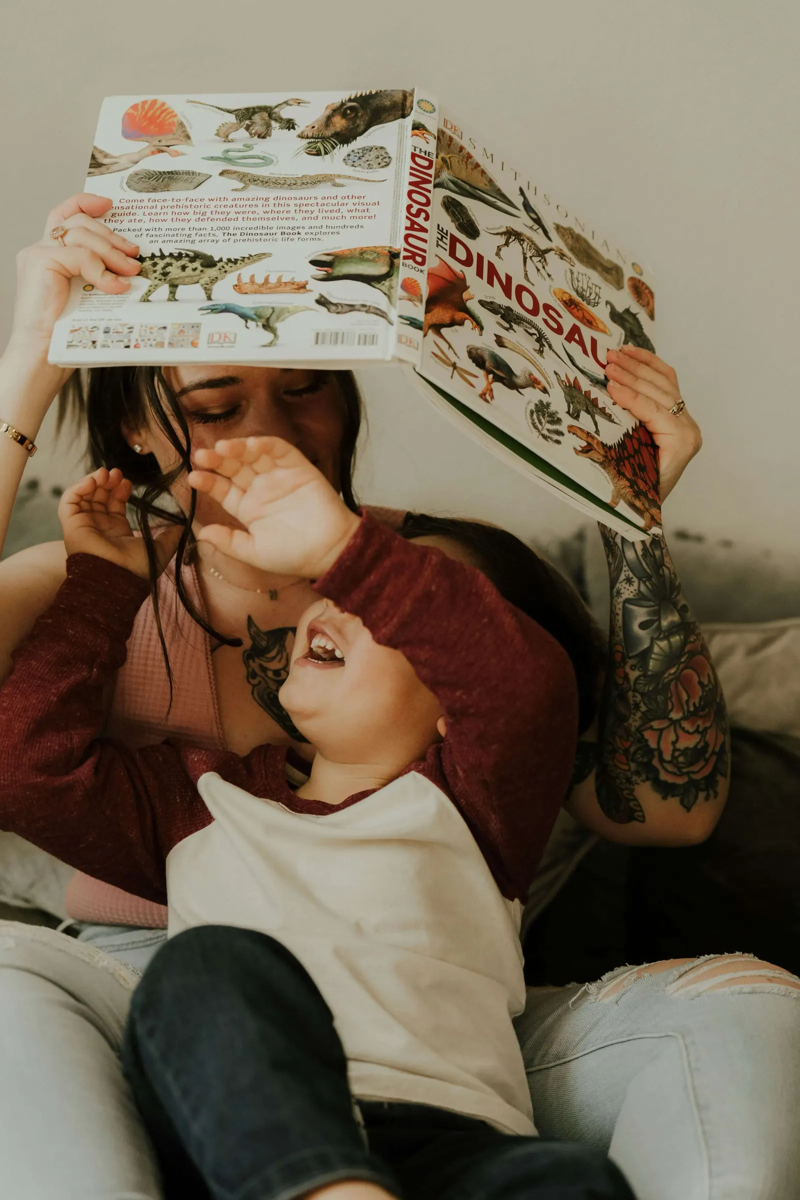 Mother and laughing toddler reading a dinosaur book together