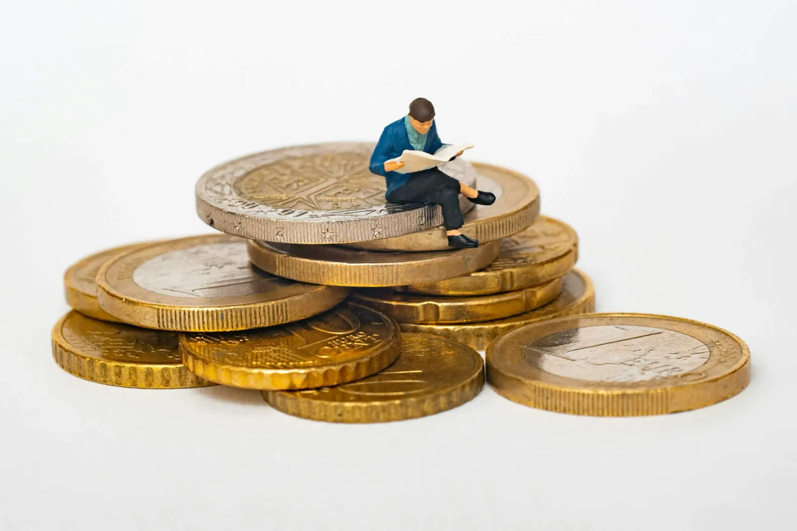 Miniature figure reading a newspaper atop a stack of euro coins