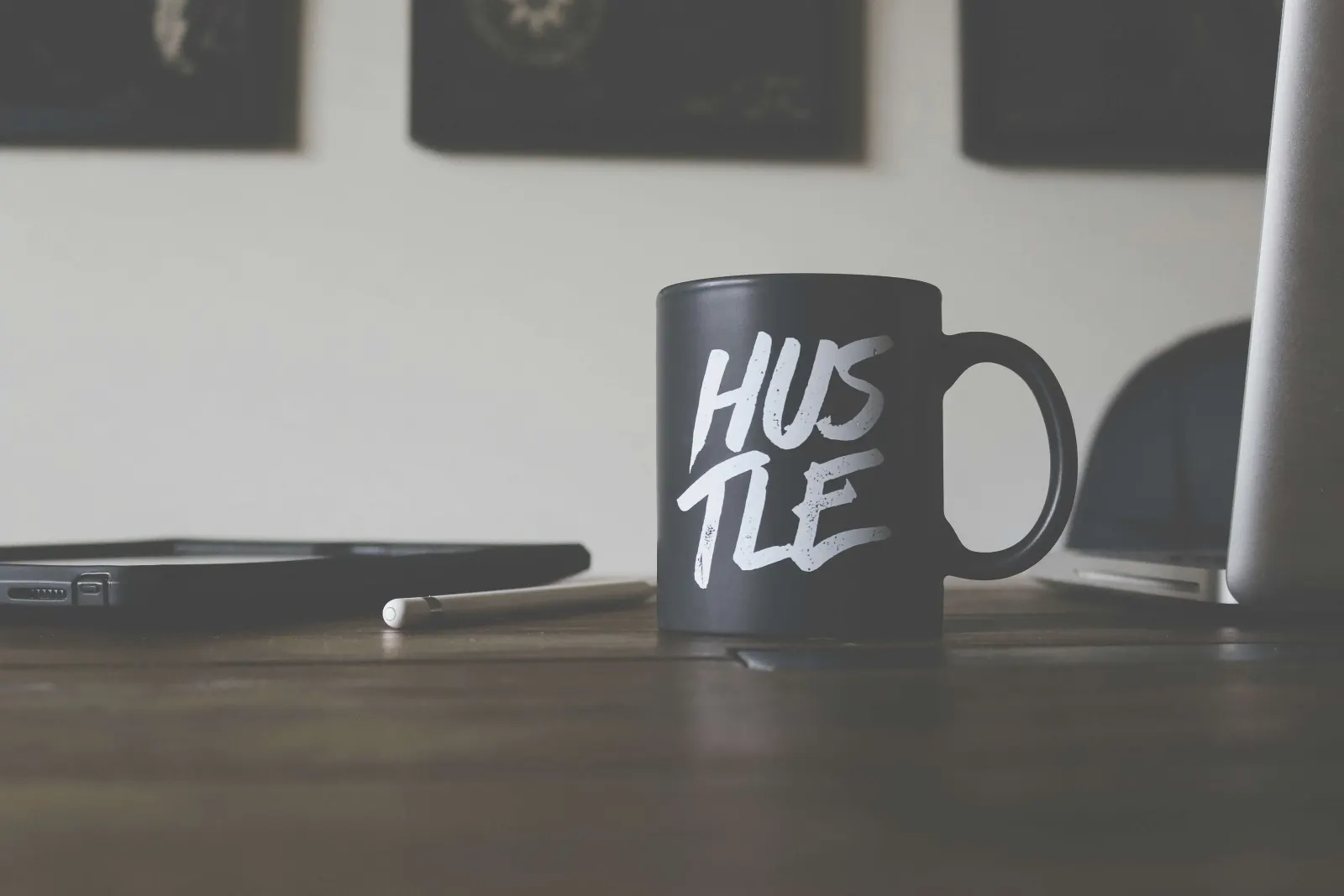 Black mug reading HUSTLE on a desk with a phone and laptop