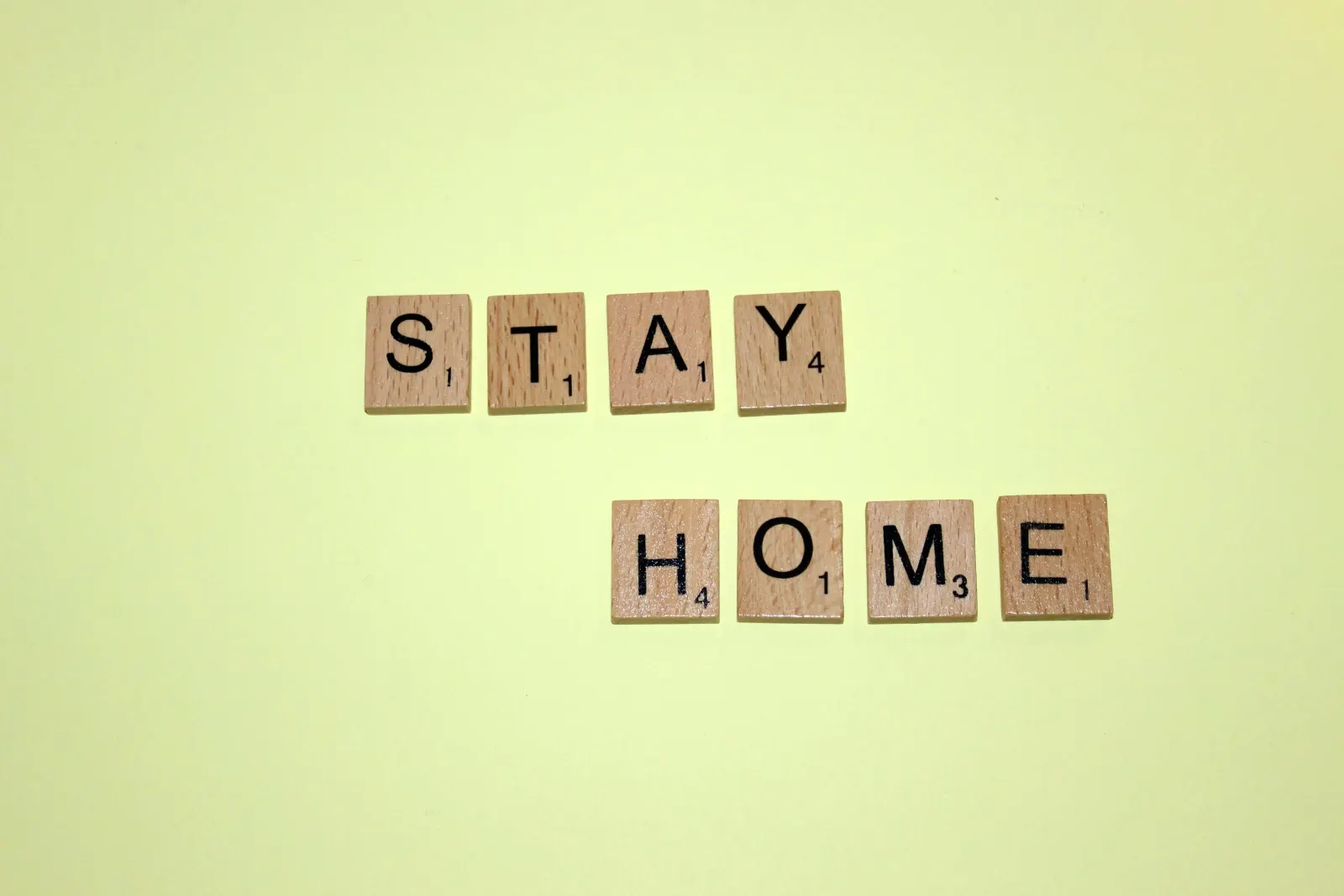 Wooden letter tiles spelling STAY HOME on a yellow background