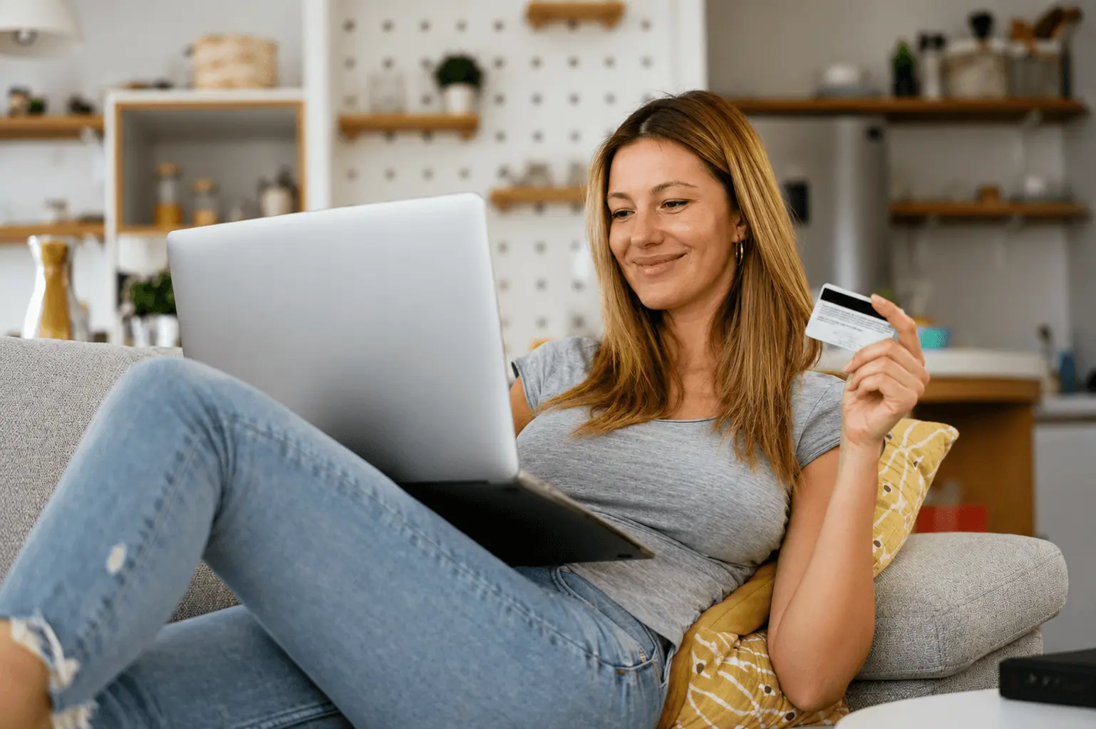 Woman on a couch using a laptop while holding a credit card