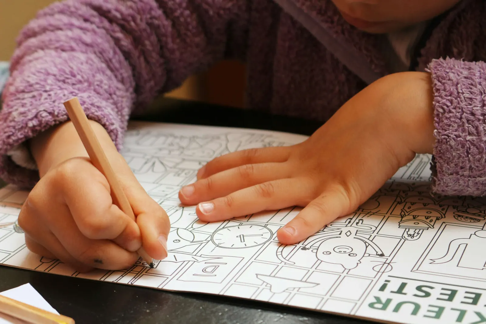 Child's hands coloring in a coloring book with a pencil