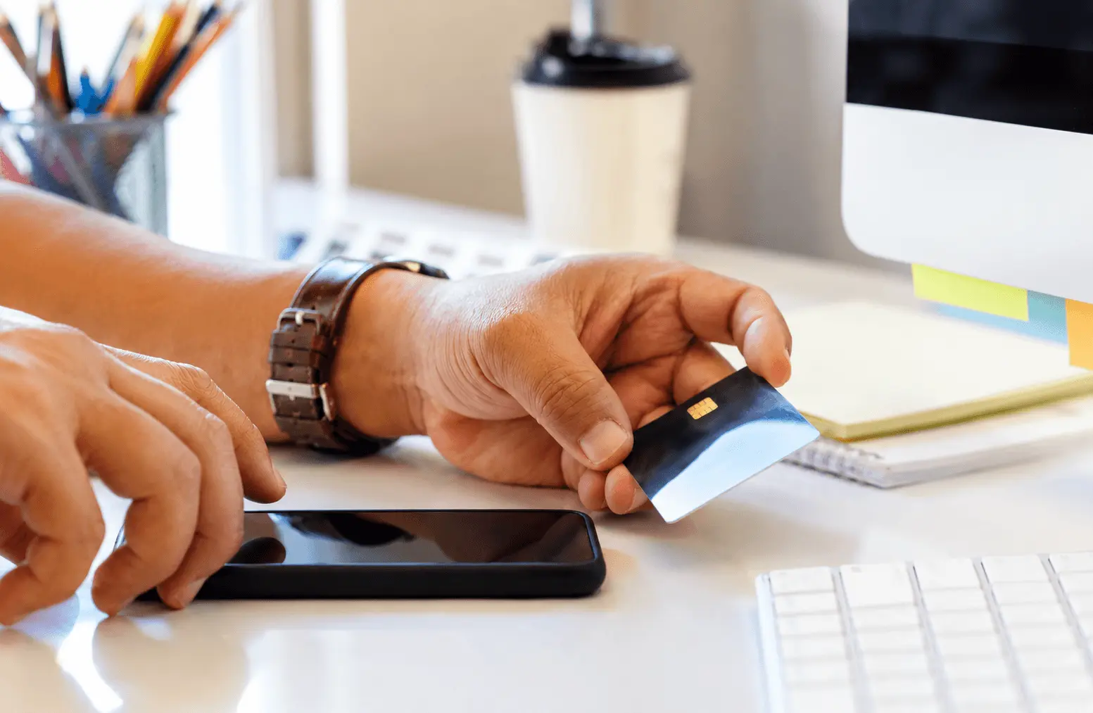 Hand holding a credit card next to a smartphone on a desk