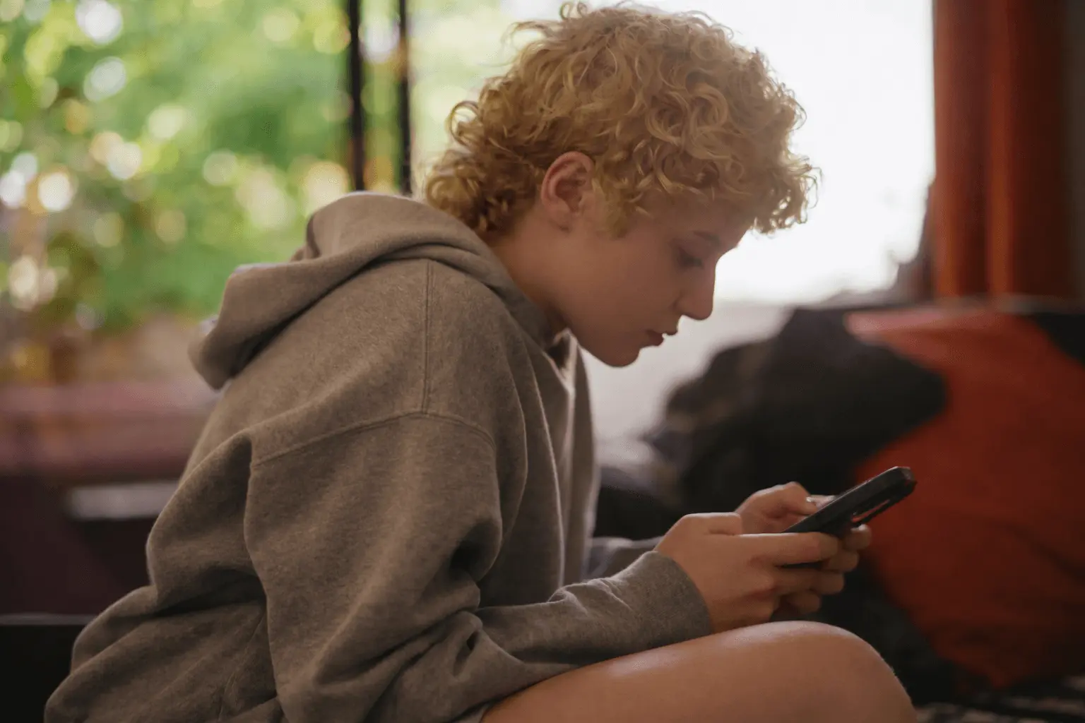 Teenager in a hoodie looking down at a phone in dim light