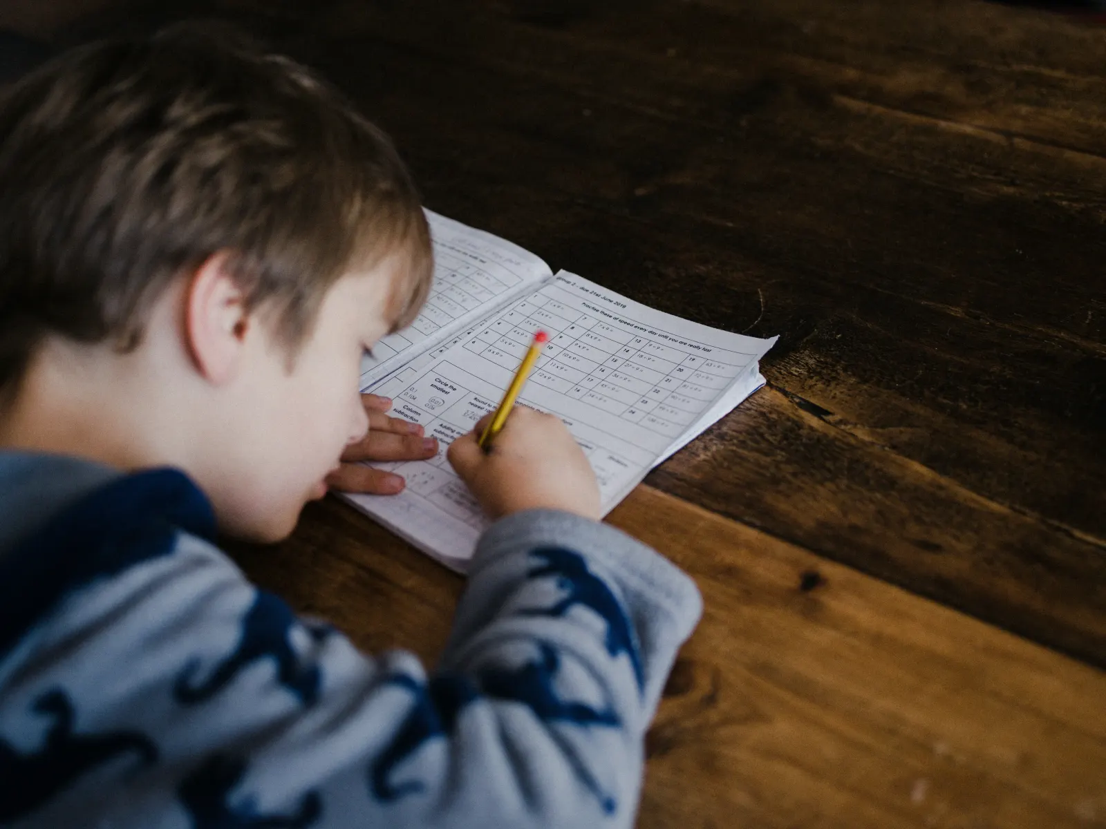 Boy leaning over a workbook doing multiplication practice with a pencil