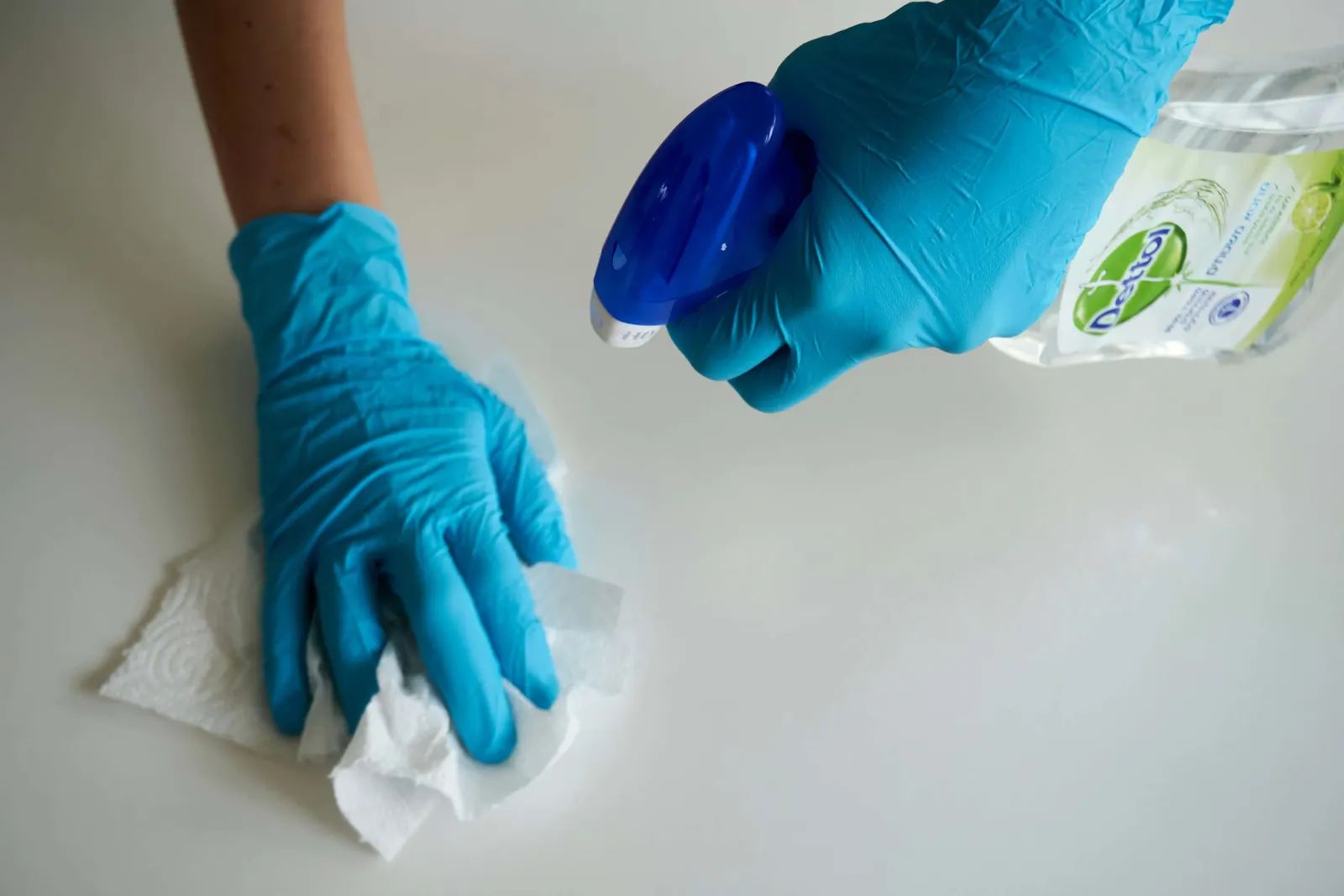 Blue-gloved hands wiping a counter with a Dettol spray bottle