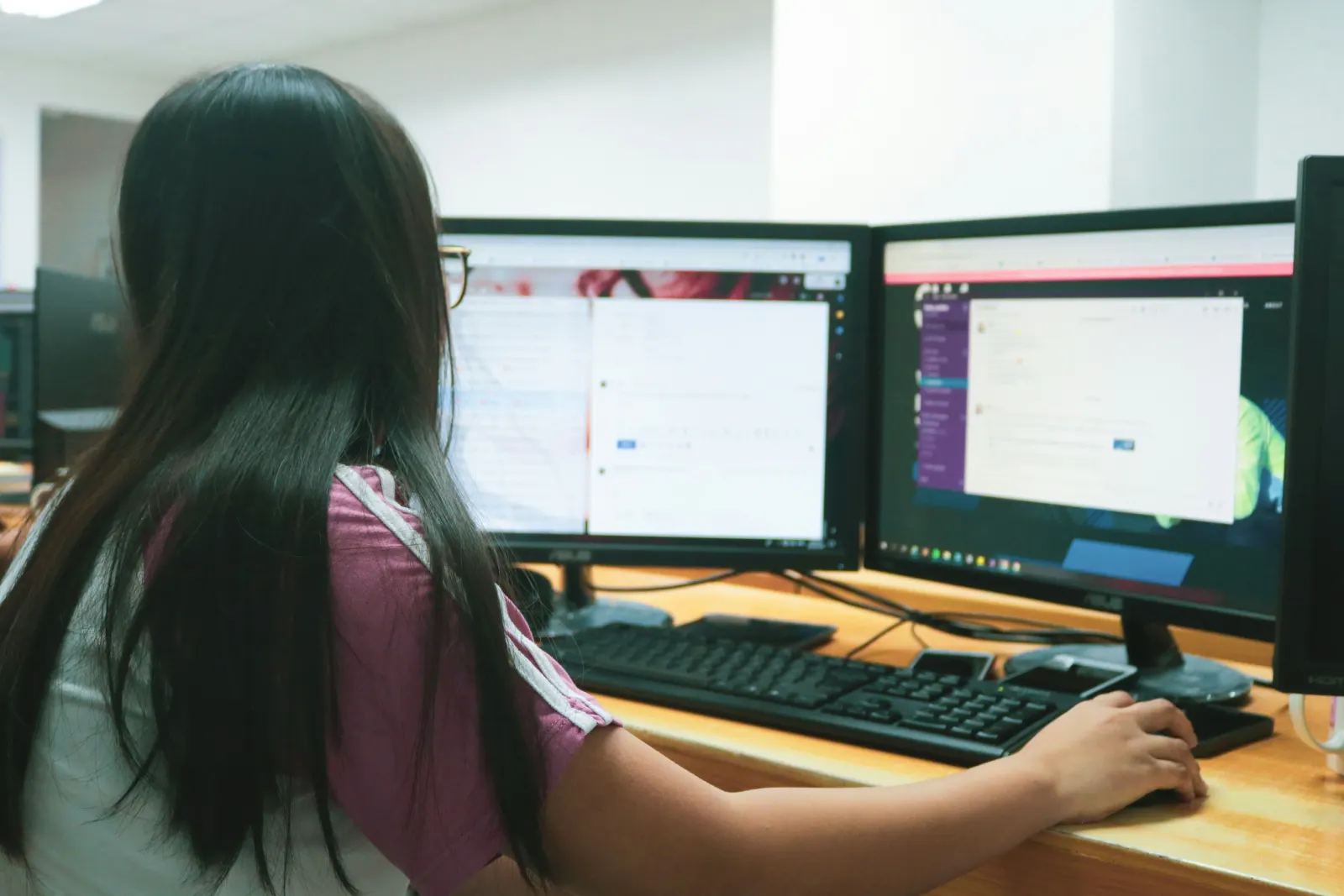 Person seen from behind typing at a desk with dual computer monitors