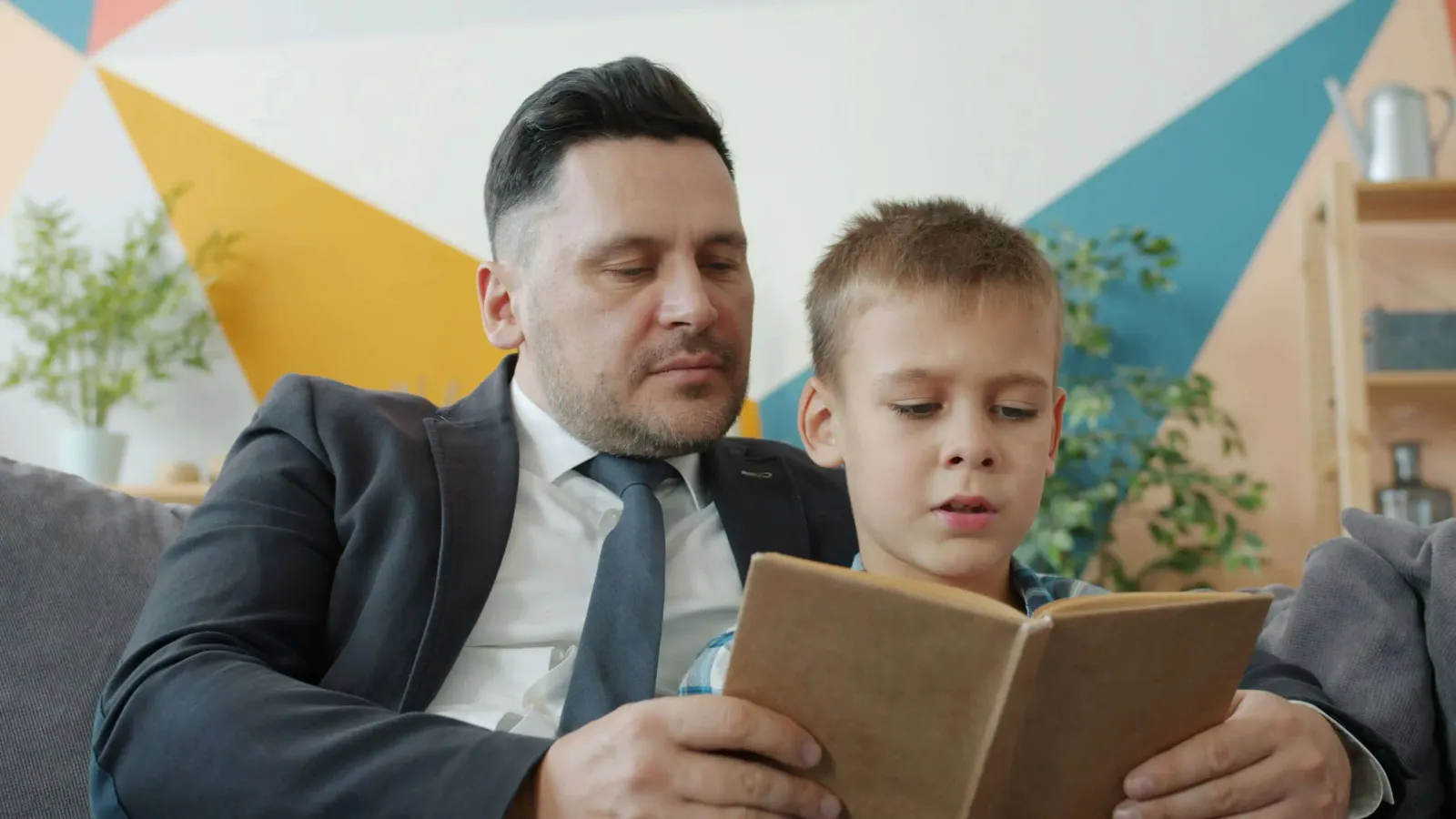 Father in a suit reading a book with his young son