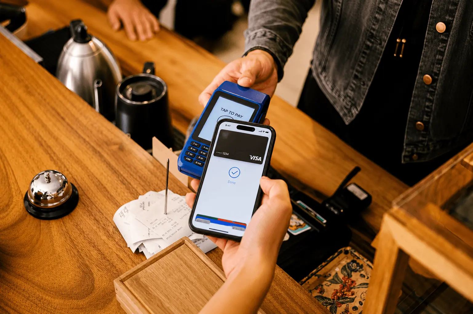 Hand tapping a phone with Apple Pay against a card reader