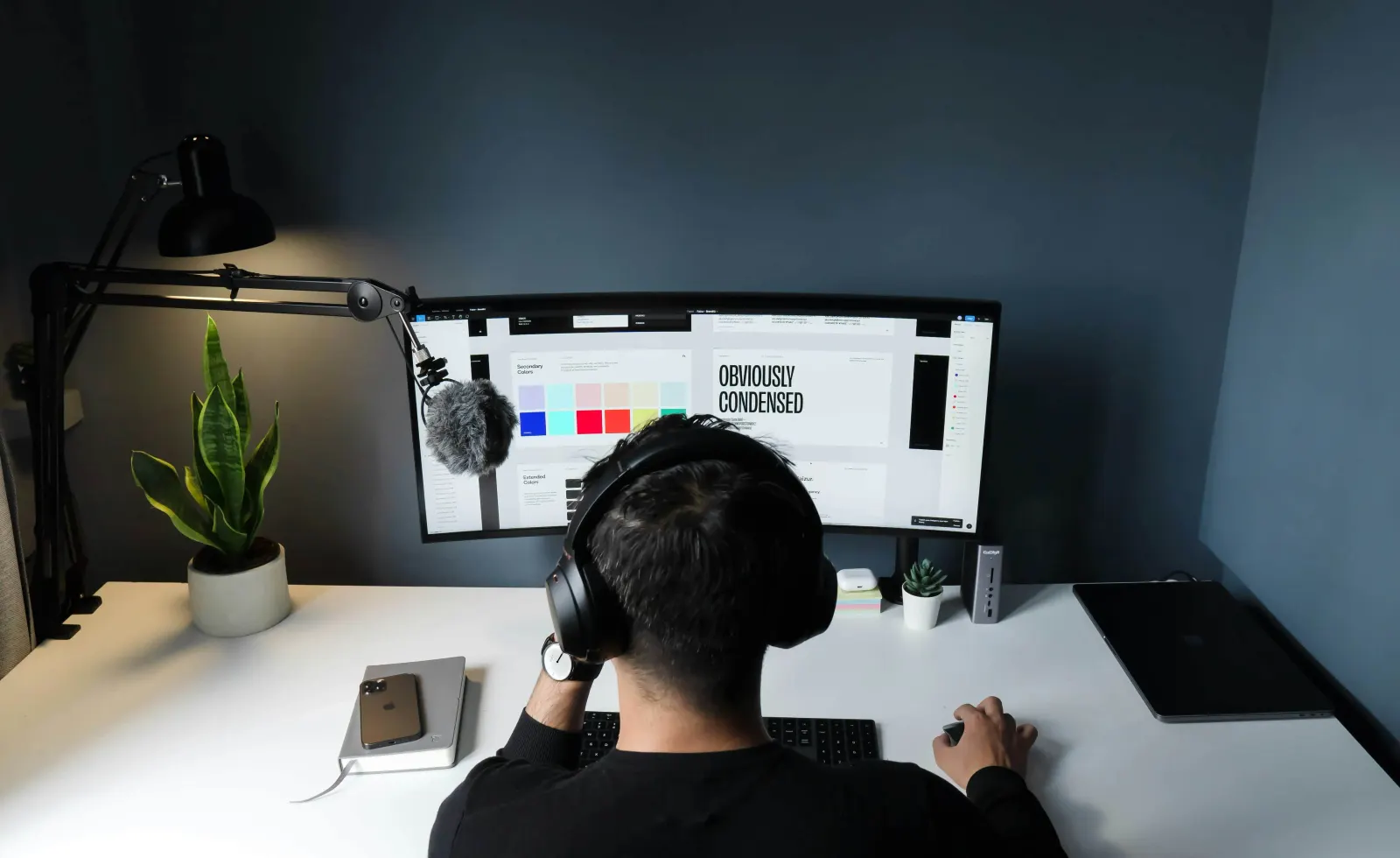 Man wearing headphones working on design software at a curved monitor