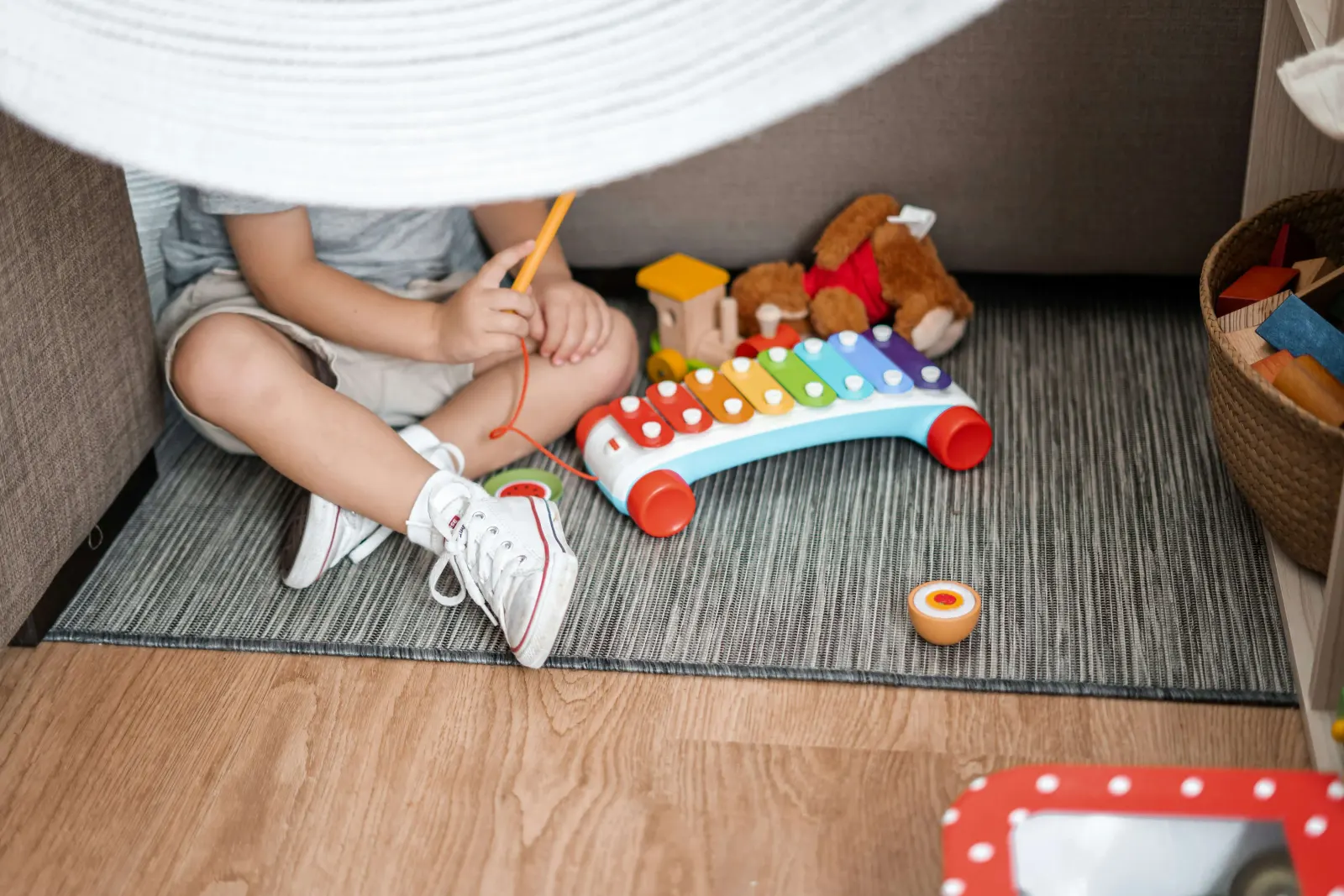 Toddler playing with a toy xylophone under a blanket fort