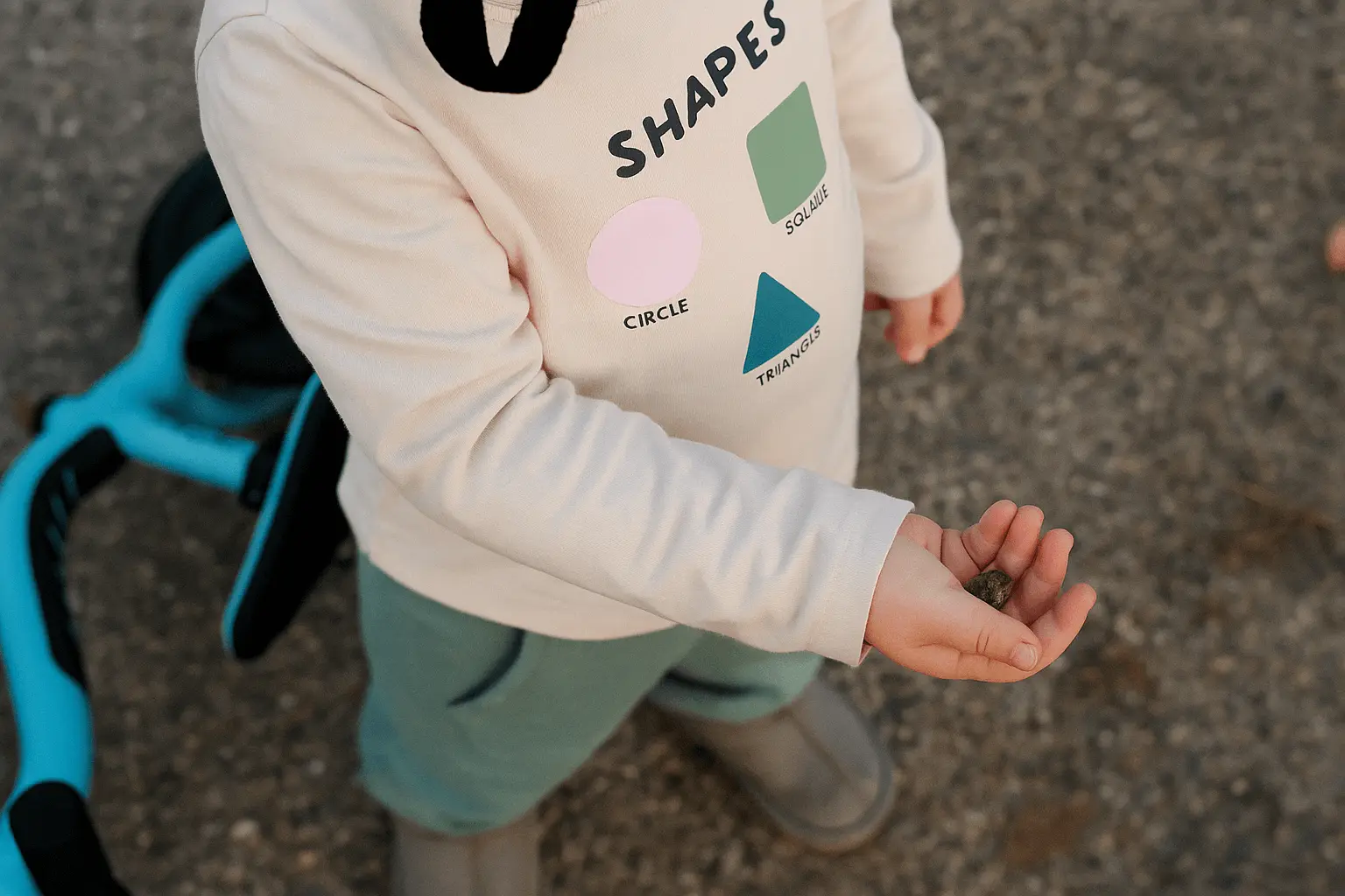 Toddler in a Shapes-print sweatshirt holding a small stone outdoors