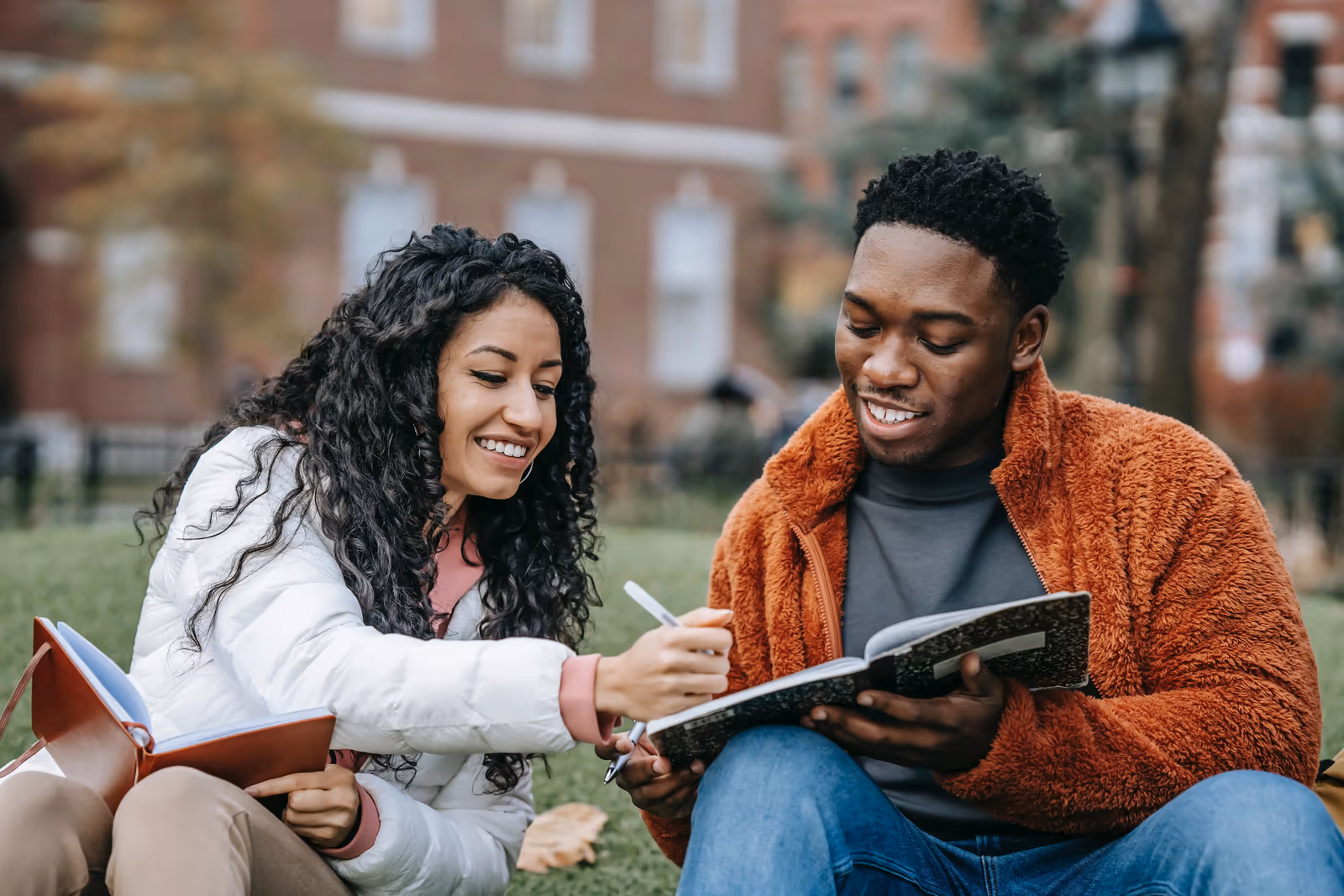 two smiling college students reviewing a notebook together on the grass