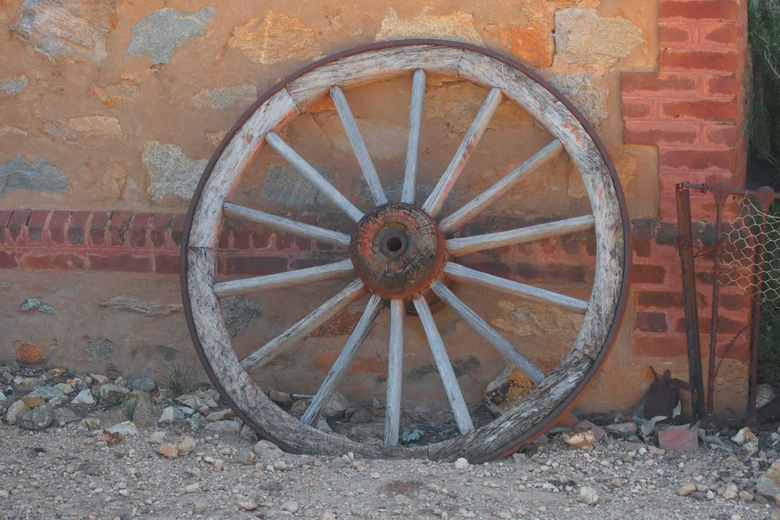 Old wooden wagon wheel leaning against a weathered stone wall
