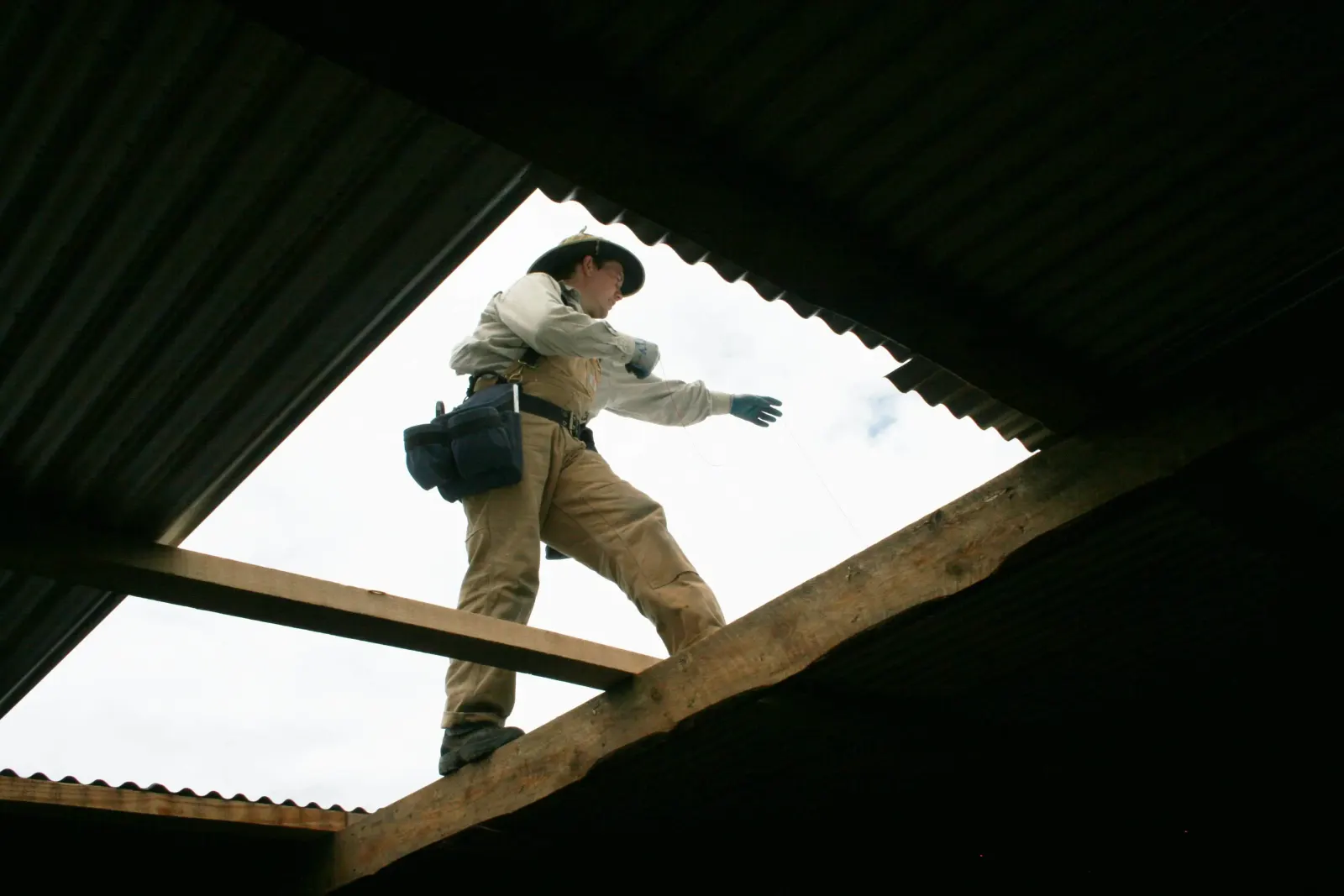 Construction worker in a wide-brim hat balancing on roof framing