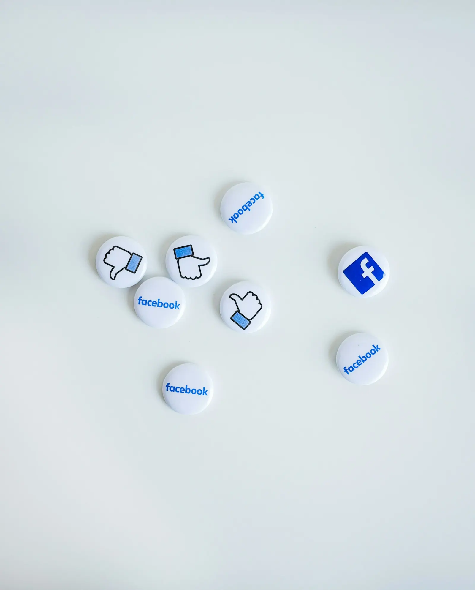 Scattered Facebook logo and thumbs-up pin badges on a white surface