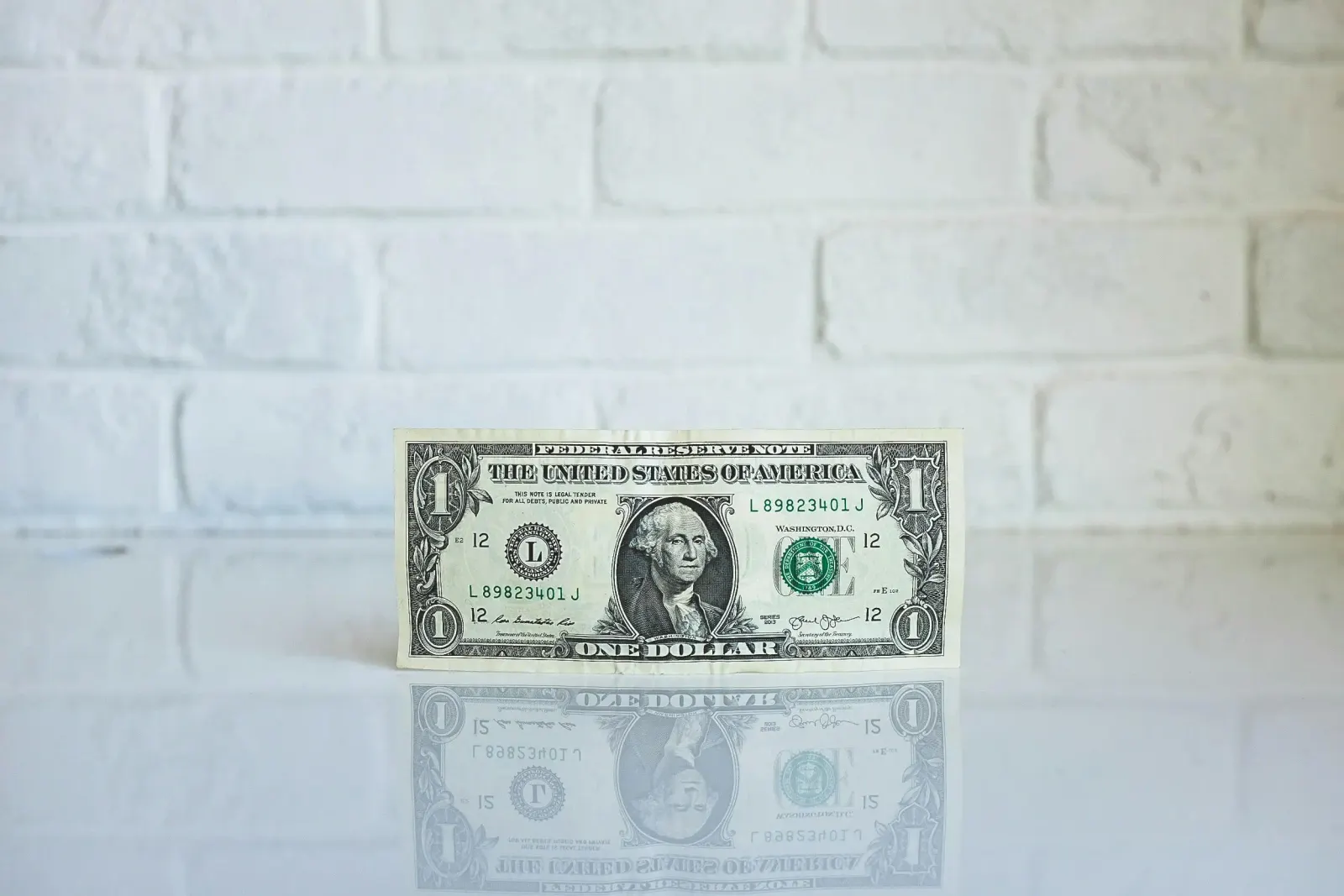 Single dollar bill standing upright against a white brick wall