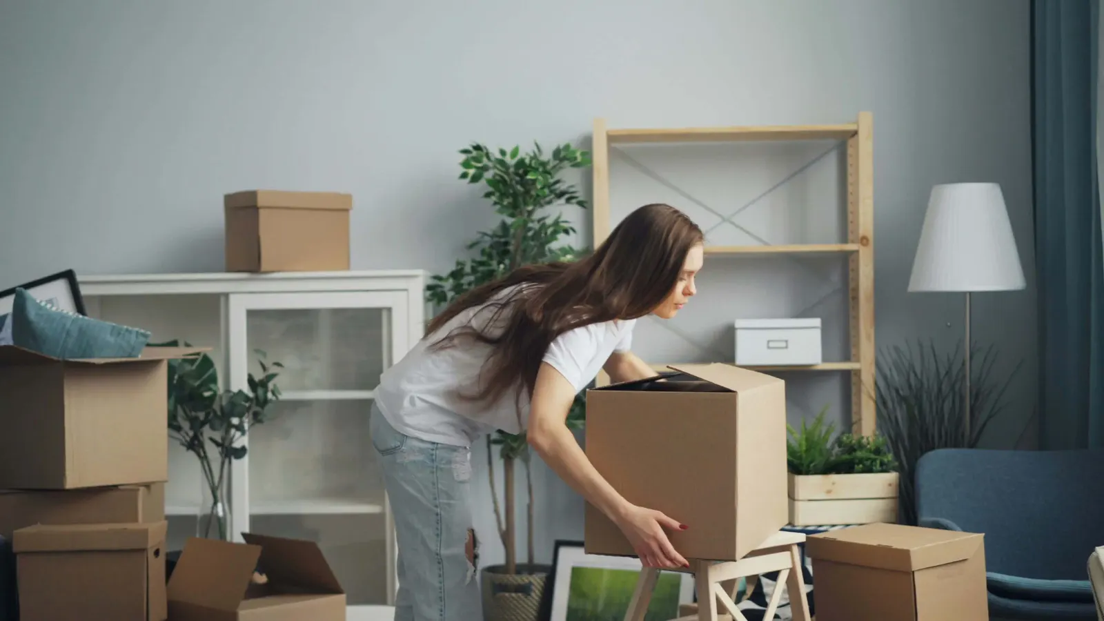 Woman lifting a cardboard box amid a room full of moving boxes