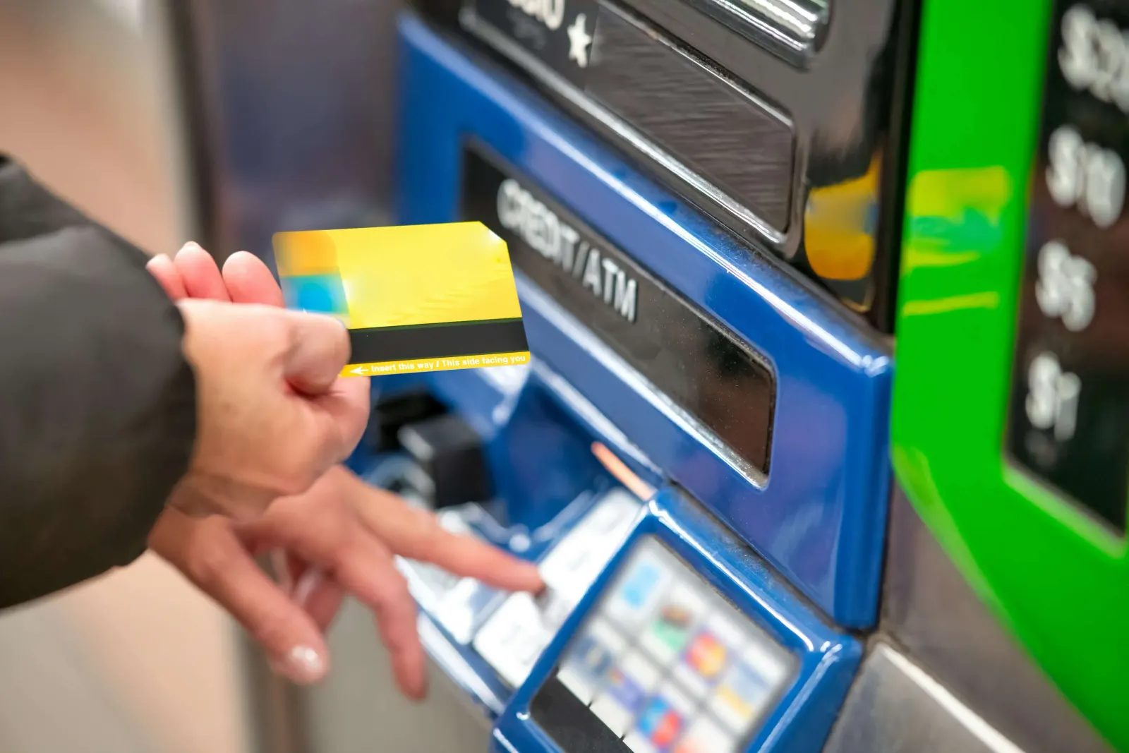 Hand inserting a yellow bank card into an ATM