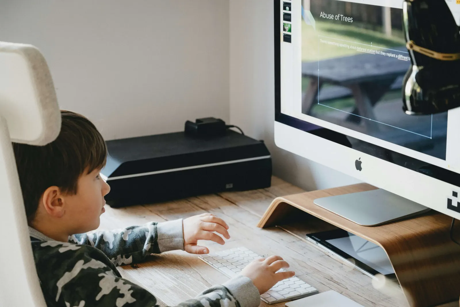 Boy typing at an iMac showing a school presentation slide