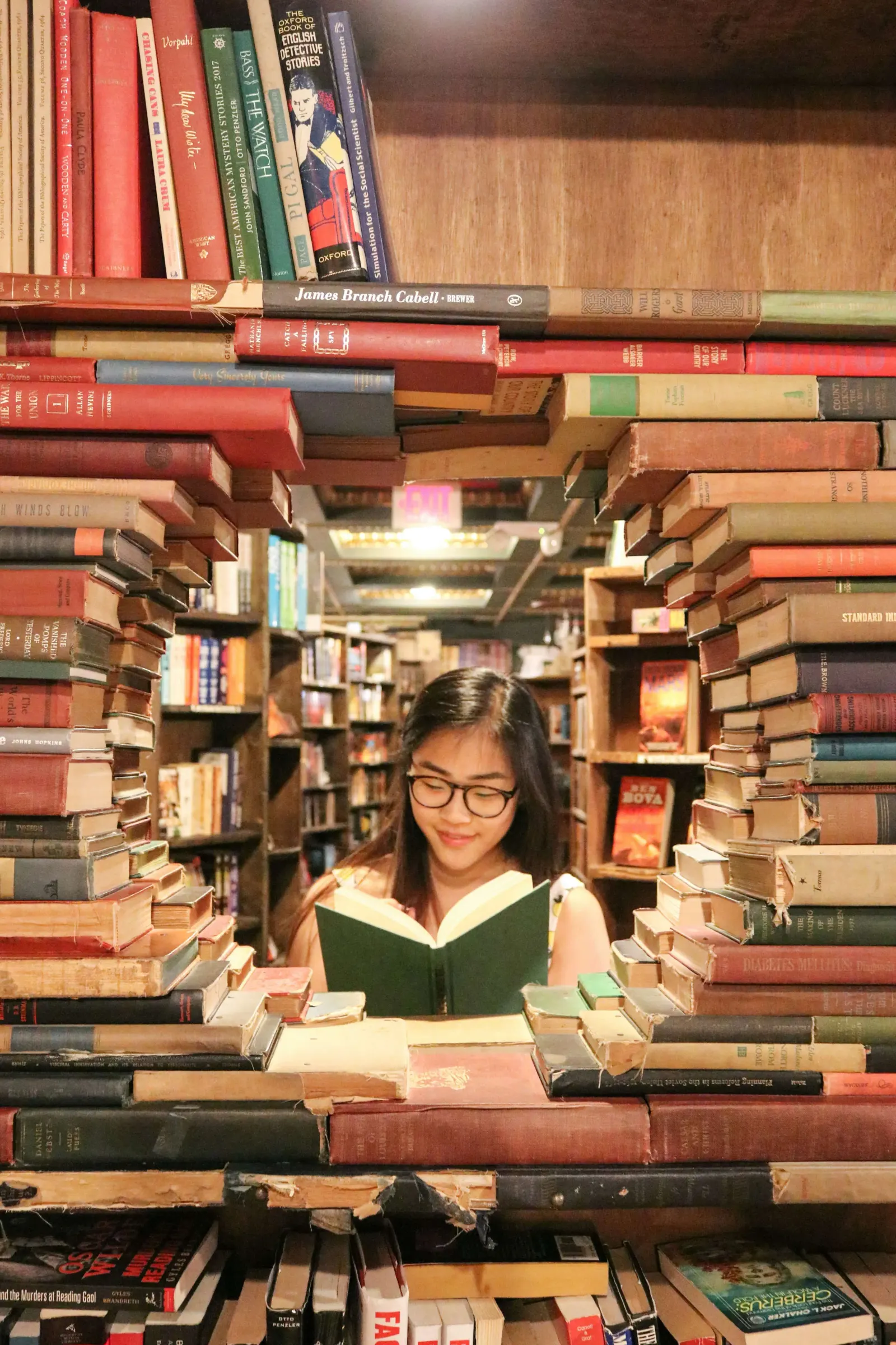 Girl reading a book inside a tunnel of stacked bookshelves