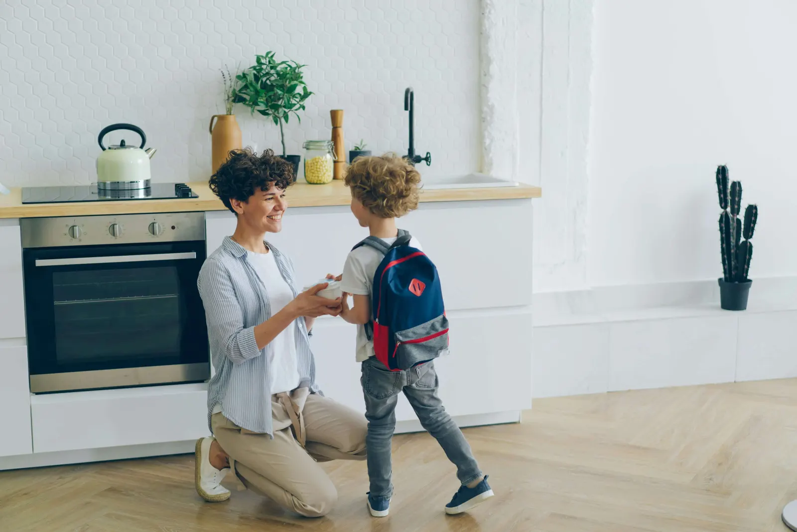 Mother kneeling to hand something to her son wearing a backpack