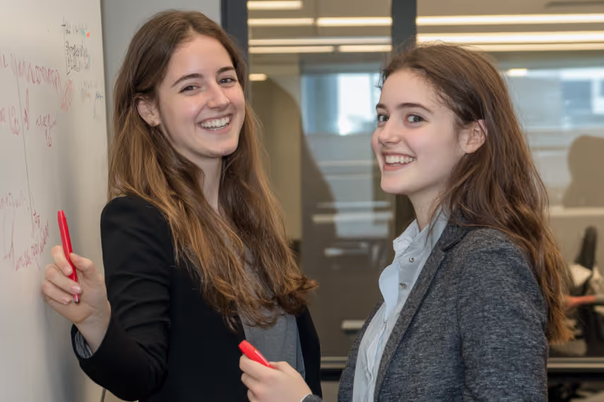 two smiling young women writing on a whiteboard together