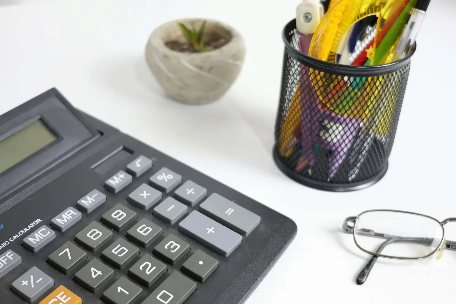 Calculator, succulent, cup of pencils, and eyeglasses on a desk