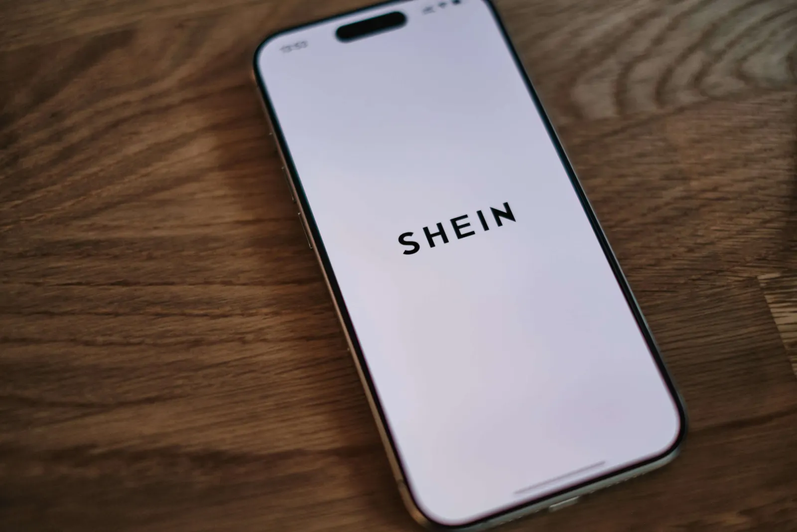 Smartphone showing the SHEIN logo splash screen on a wood table