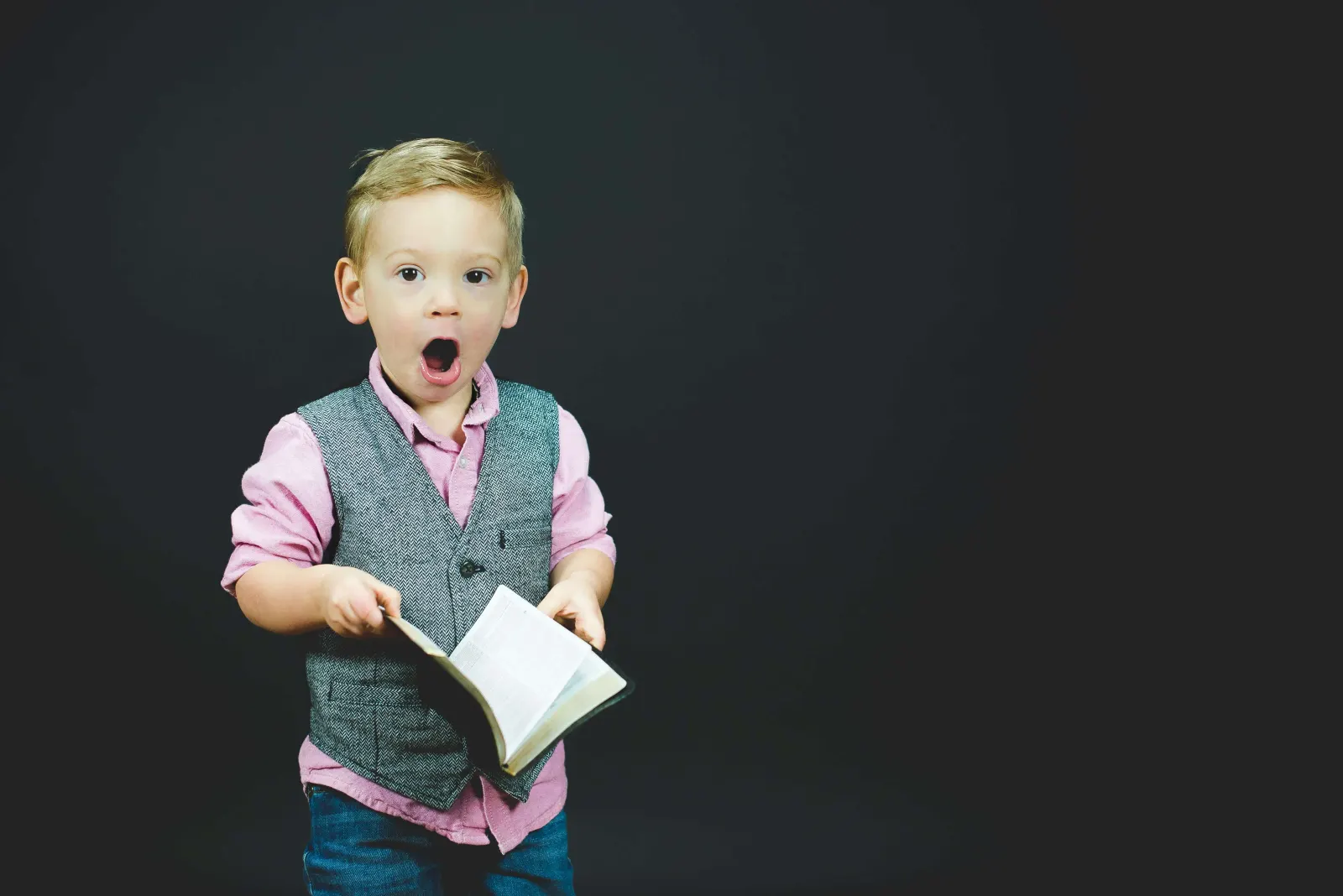 Young boy in a vest making a surprised face while holding an open book