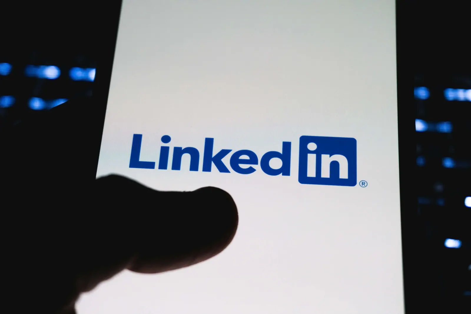 LinkedIn logo on a phone screen held by a silhouetted hand