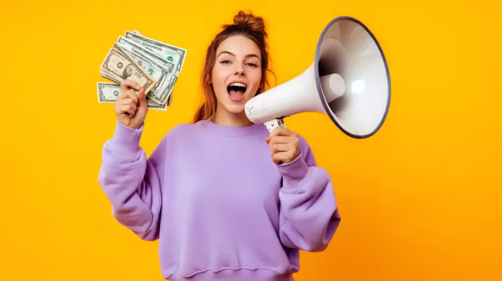 woman in a purple hoodie holding cash and shouting into a megaphone