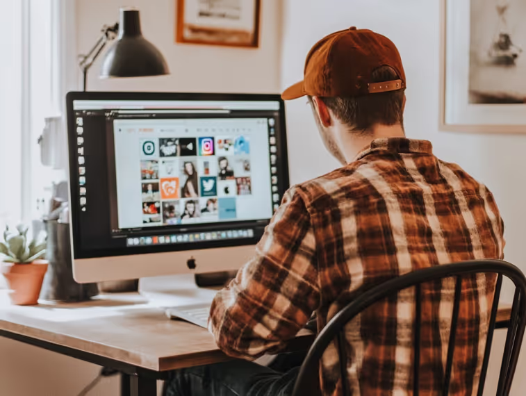 Man in a cap browsing social media app icons on a desktop monitor
