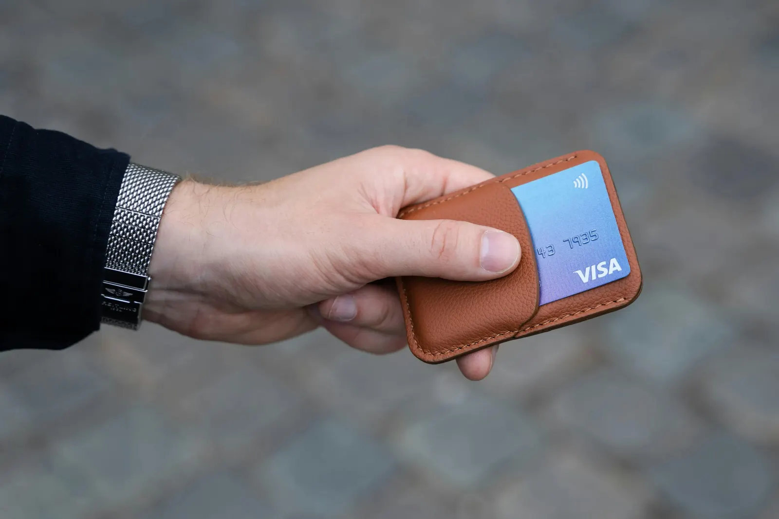 Hand holding a brown wallet with a blue Visa card tucked in