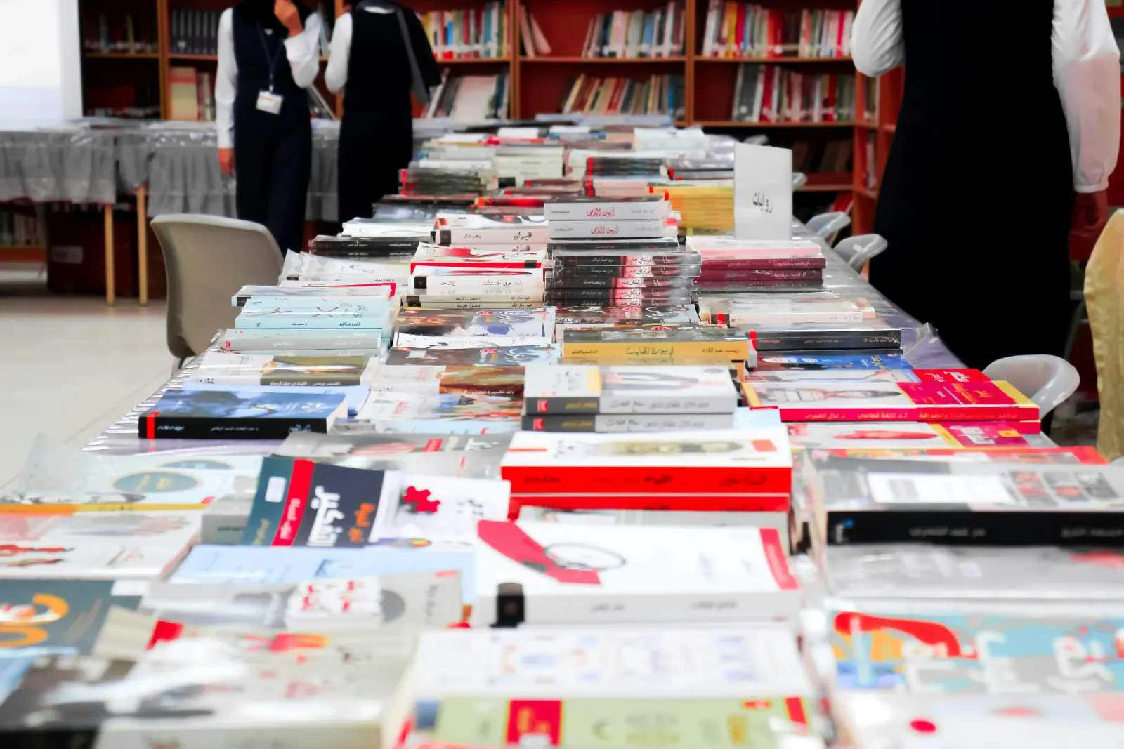 Long library tables piled with books, students browsing in the background
