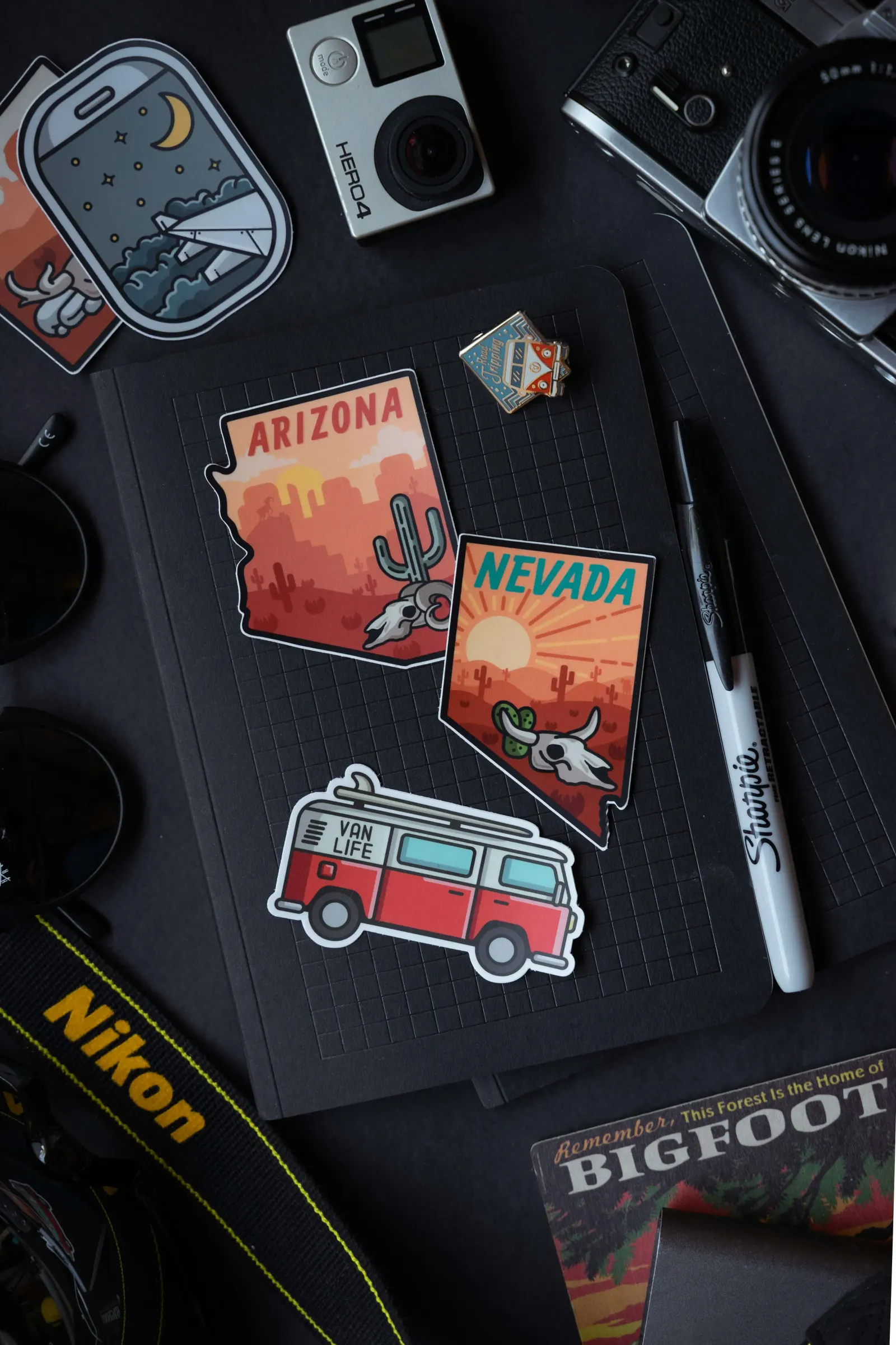 Arizona and Nevada travel stickers and a van life sticker on a notebook with camera gear