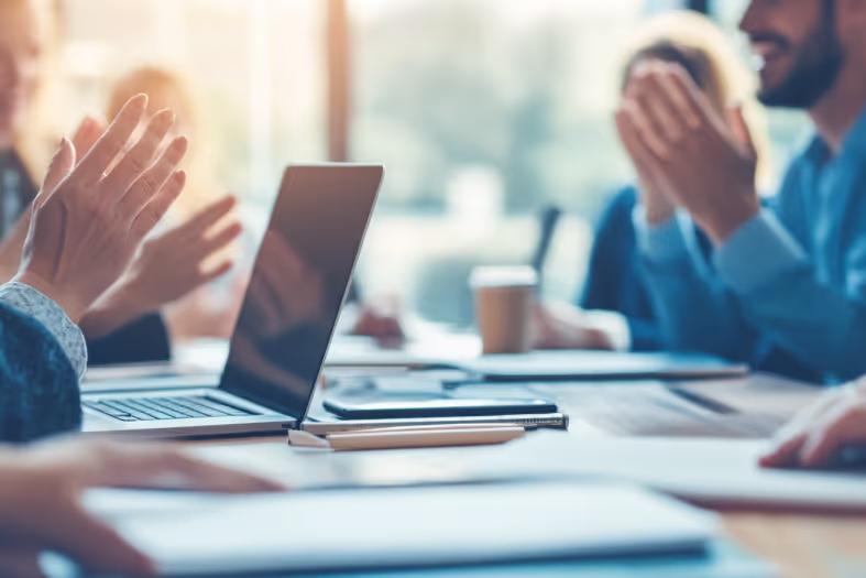 Hands clapping near an open laptop at a meeting table