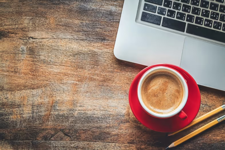 Overhead view of a red espresso cup beside a laptop and pencils
