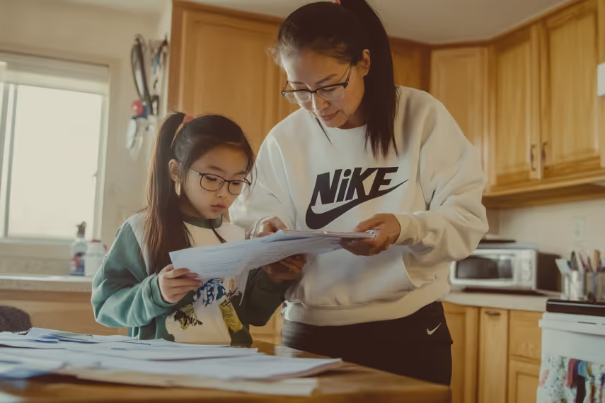 Mother in a Nike sweatshirt reviewing papers with her daughter in a kitchen