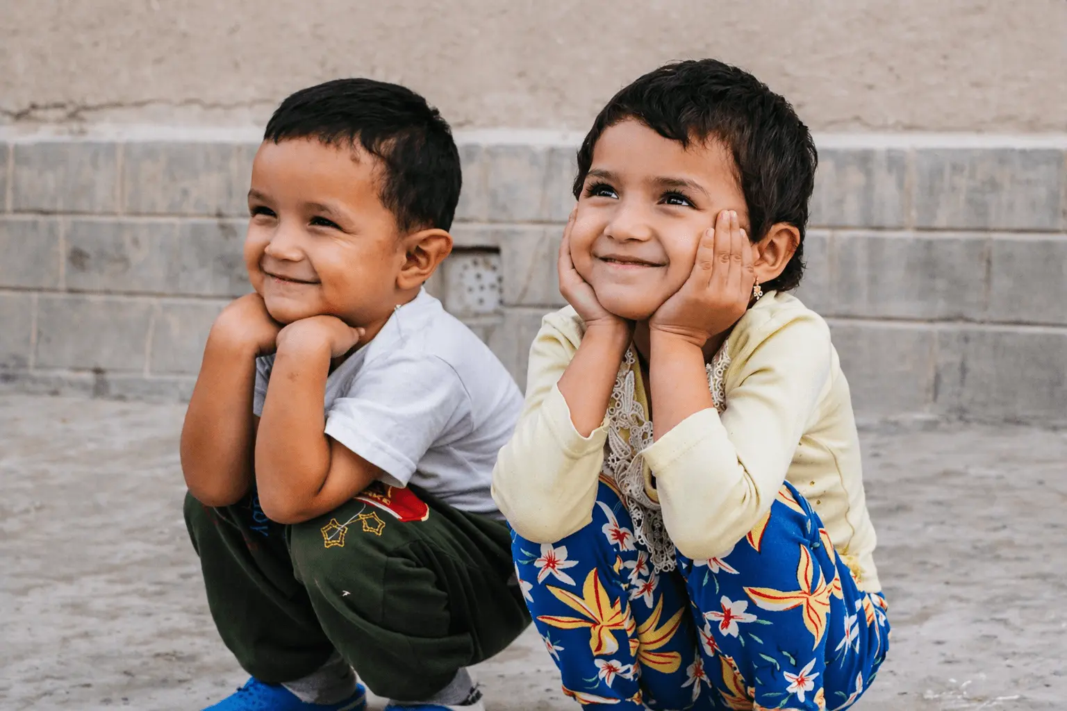 two smiling young children crouching together with hands on their cheeks