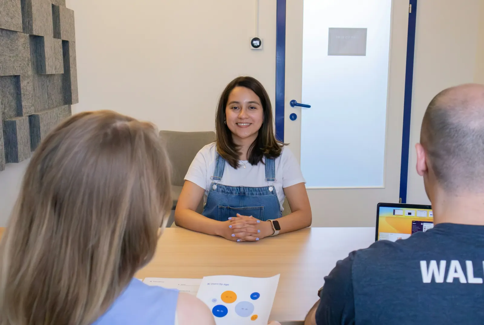 Woman smiling across a table from two interviewers with a laptop